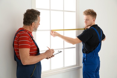 Service men measuring window for installation indoors