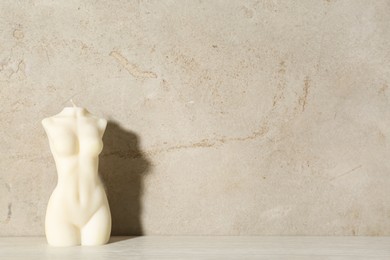 Photo of Beautiful female body shaped candle on table near light wall, space for text