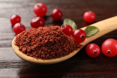 Photo of Dried cranberry powder in spoon, fresh berries and green leaves on wooden table, closeup