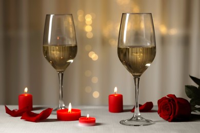 Photo of Glasses of white wine, rose flower and burning candles on grey table against blurred lights. Romantic atmosphere