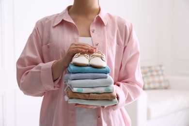 Photo of Woman holding stack of baby's clothes and small shoes indoors, closeup