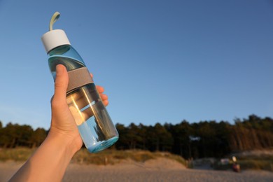 Photo of Woman holding glass bottle with water against blue sky, closeup. Space for text