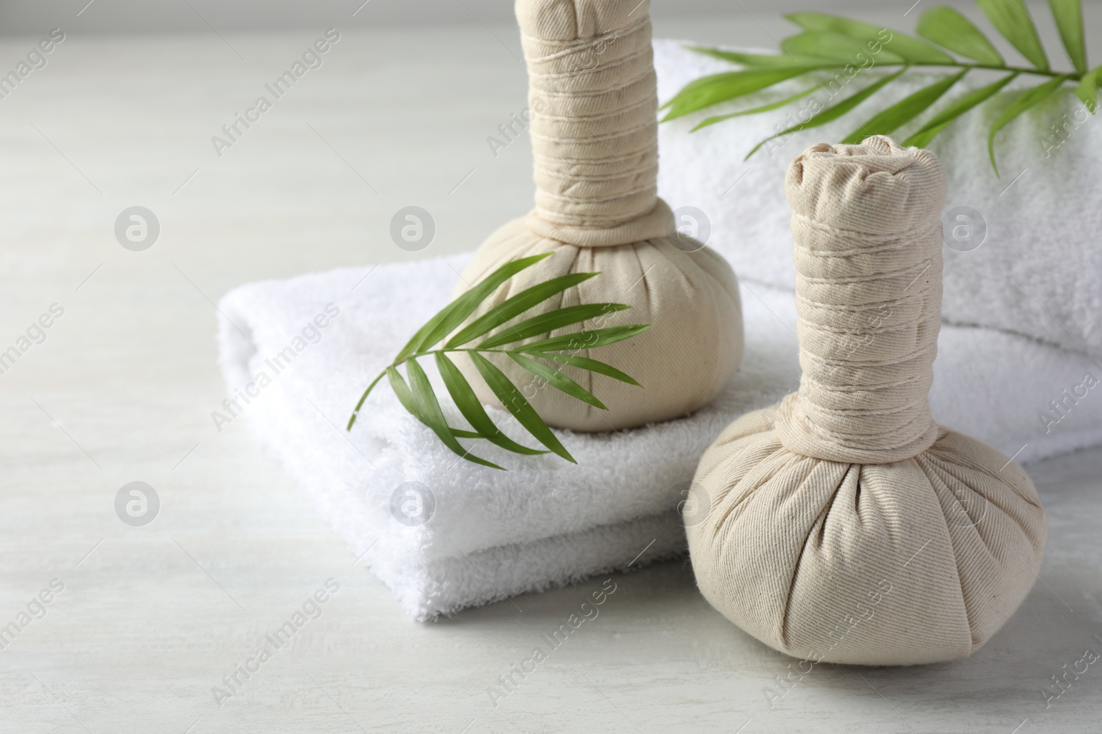 Photo of Spa composition. Herbal bags, towels and palm leaves on light table, space for text