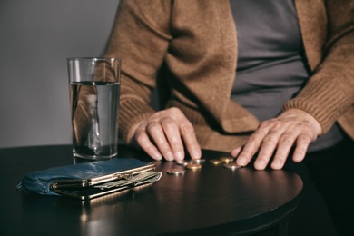 Photo of Poor senior woman with water, wallet and coins at table, closeup