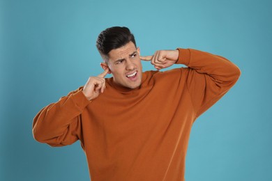 Photo of Emotional man covering ears with fingers on light blue background