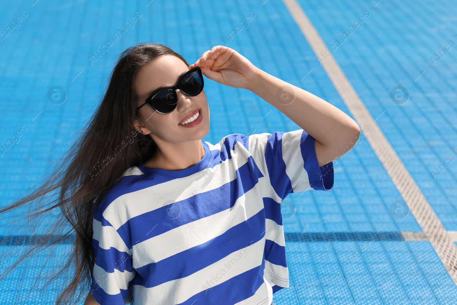 Photo of Beautiful smiling woman in sunglasses on blue floor covering outdoors, space for text