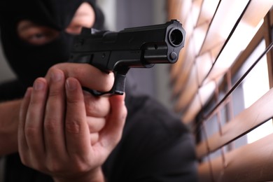 Man in mask aiming through window blinds indoors, focus on hands