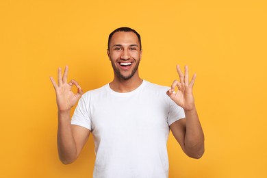 Smiling African American man showing ok gesture on orange background
