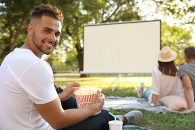 Young man with popcorn watching movie in open air cinema. Space for text