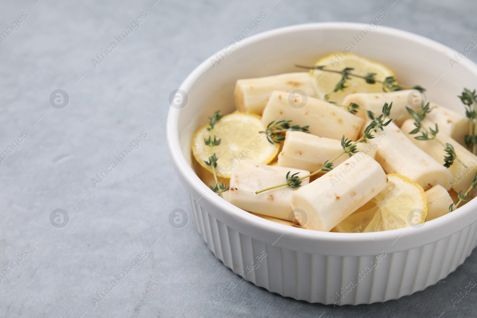 Photo of Dish with raw salsify roots, lemon and thyme on light grey table, closeup. Space for text