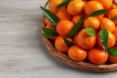 Photo of Fresh ripe juicy tangerines and green leaves on white wooden table, space for text