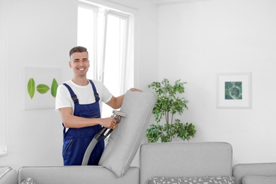 Photo of Dry cleaning worker removing dirt from sofa cushion indoors