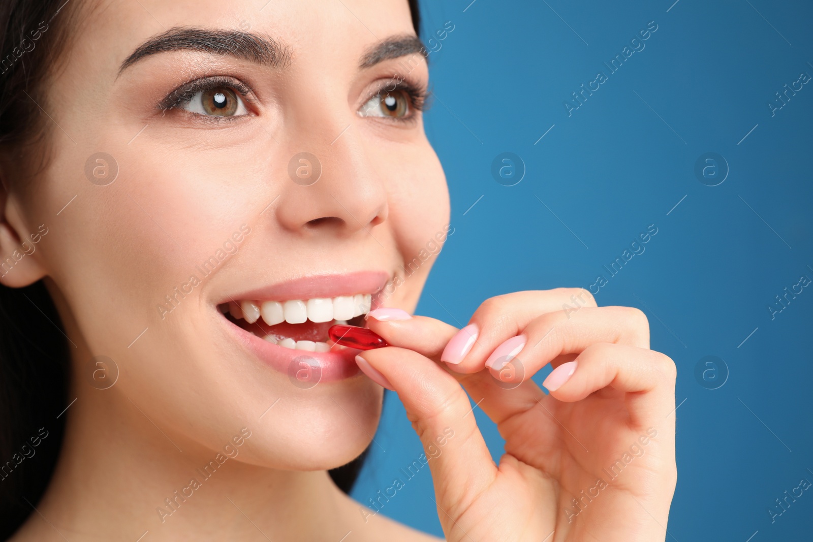 Photo of Young woman taking vitamin capsule on light blue background, closeup