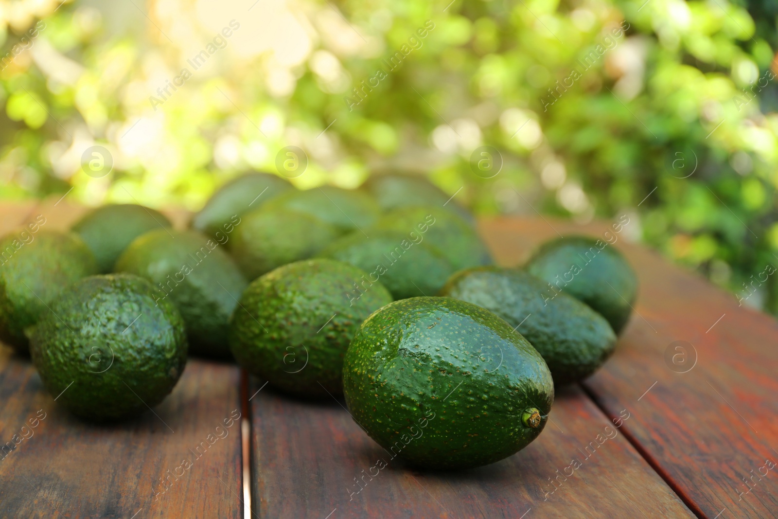 Photo of Tasty ripe avocados on wooden table outdoors