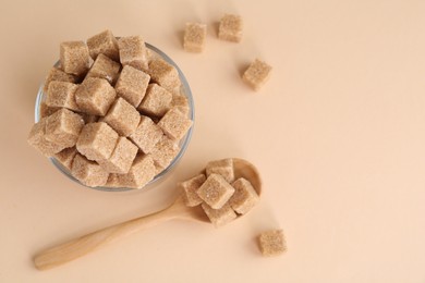 Photo of Brown sugar cubes in glass and spoon on beige background, flat lay. Space for text