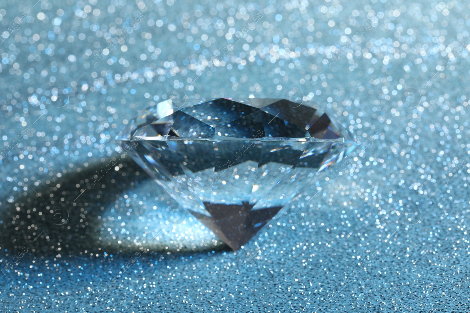 Photo of Beautiful dazzling diamond on blue glitter background, closeup
