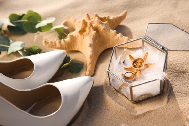 Photo of Composition with gold wedding rings on sandy beach