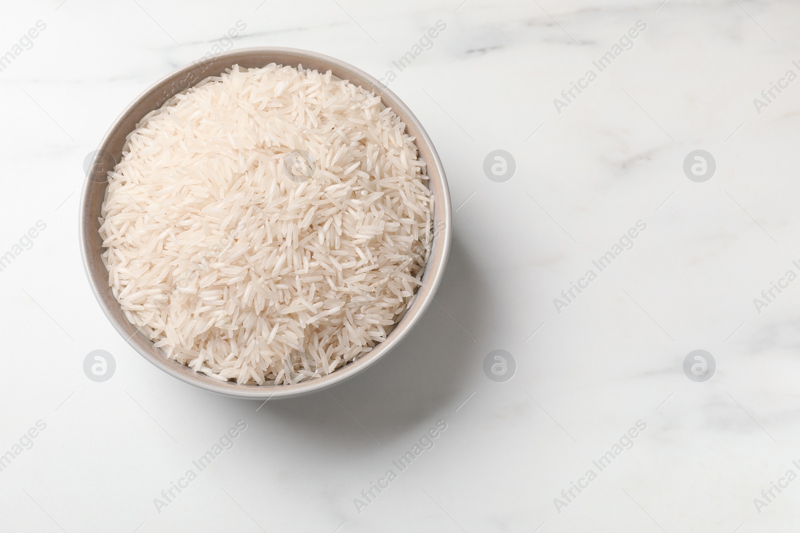 Photo of Raw basmati rice in bowl on white marble table, top view. Space for text