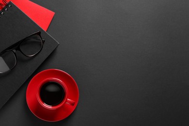 Photo of Red cup with aromatic coffee, notepads and glasses on black background, flat lay. Space for text