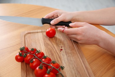 Photo of Woman cut finger with knife while cooking at wooden table, closeup