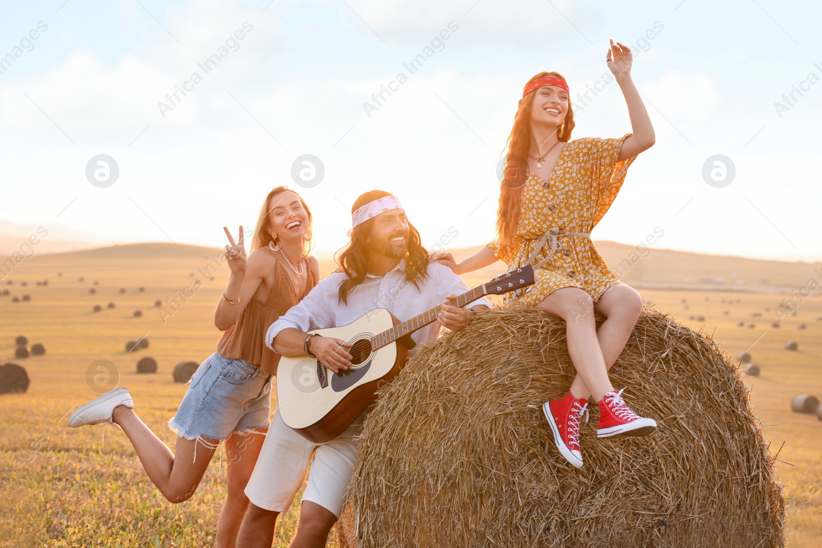 Photo of Beautiful hippie women listening to their friend playing guitar in field