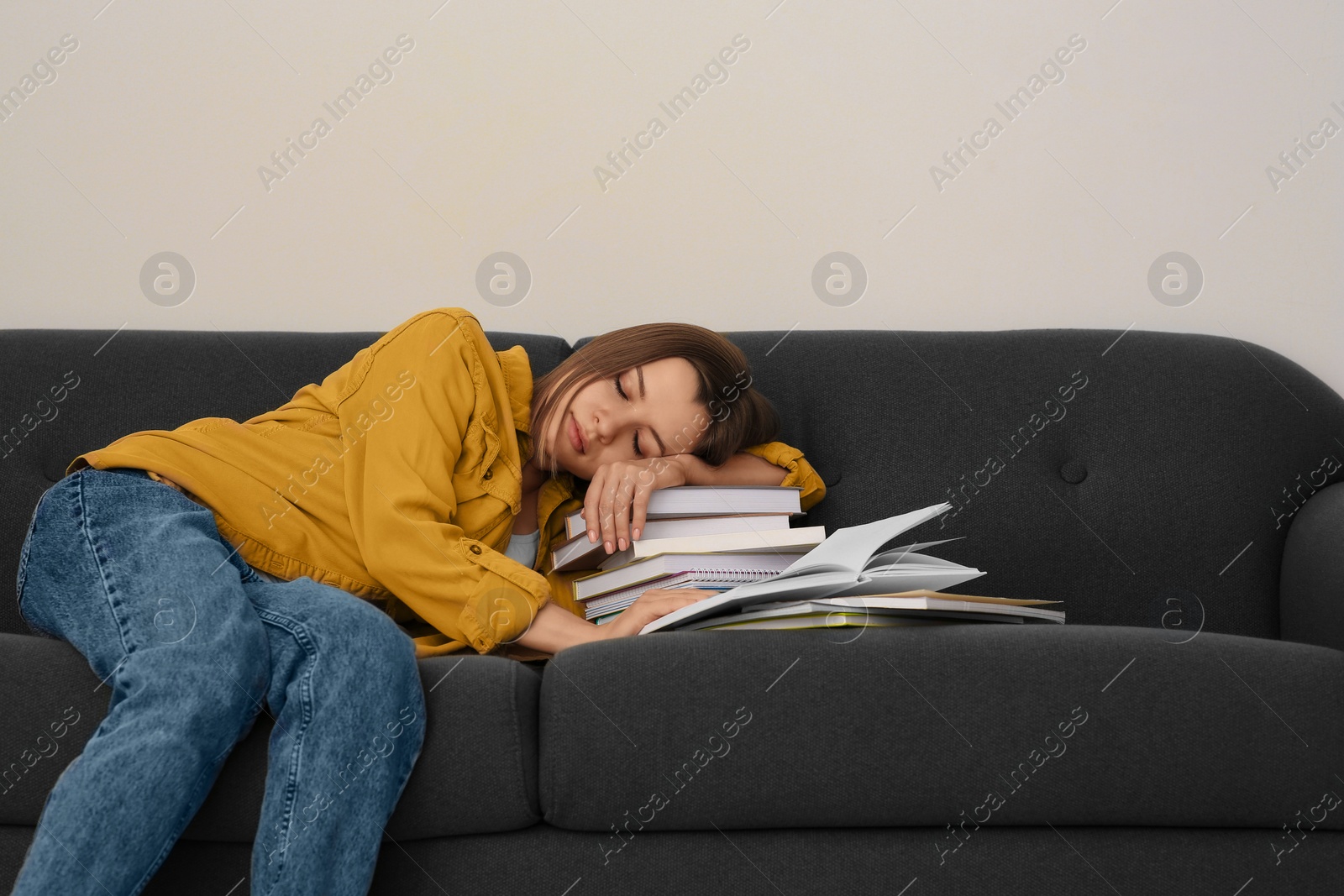 Photo of Young tired woman sleeping near books on couch indoors