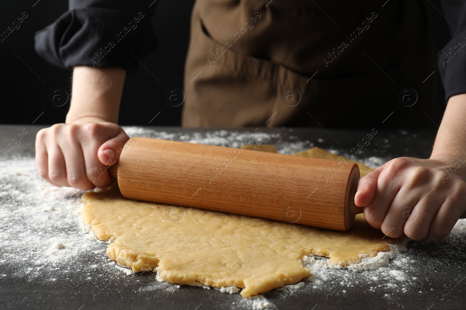 Photo of Making shortcrust pastry. Woman rolling raw dough at grey table, closeup