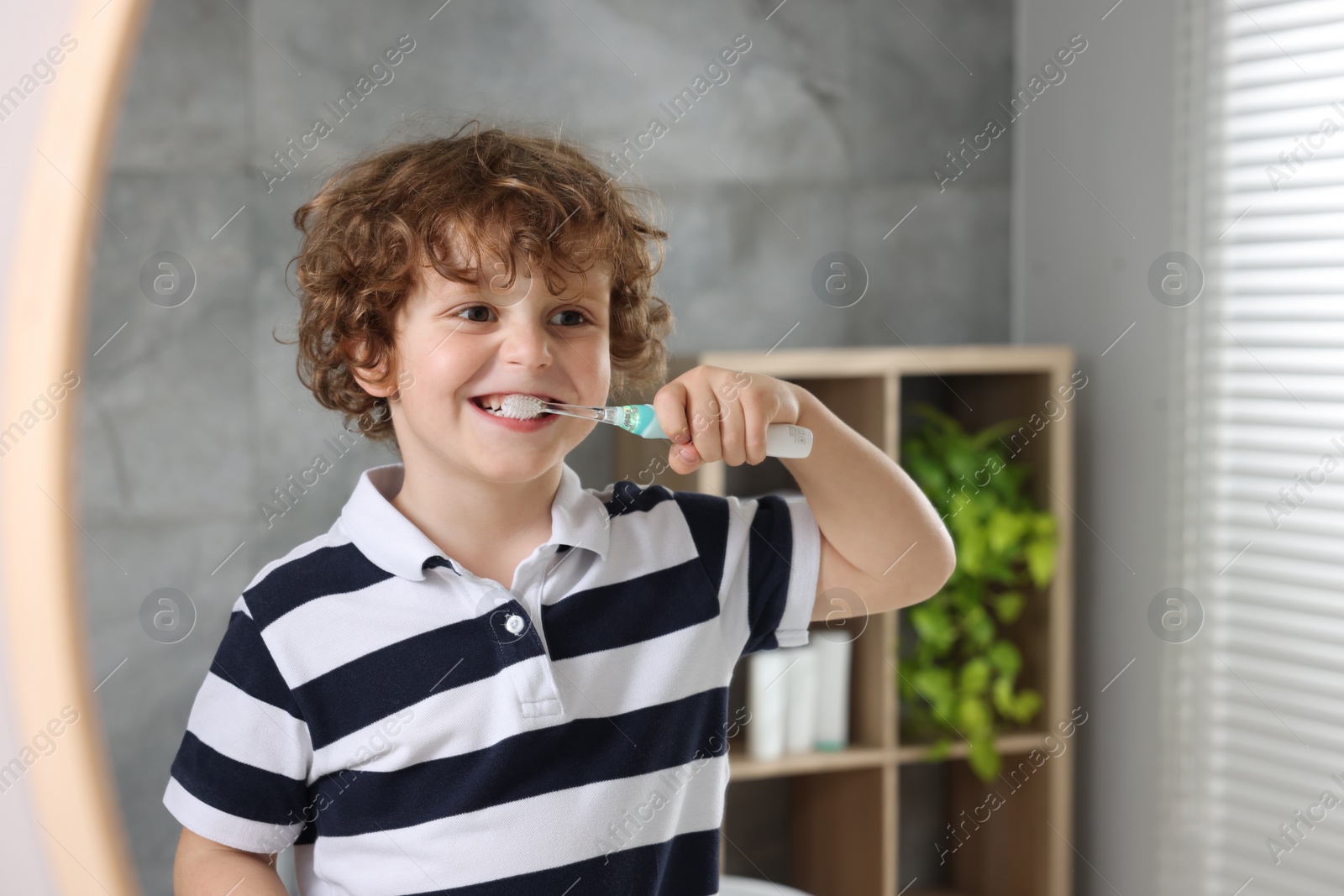 Photo of Cute little boy brushing his teeth with electric toothbrush near mirror in bathroom, space for text