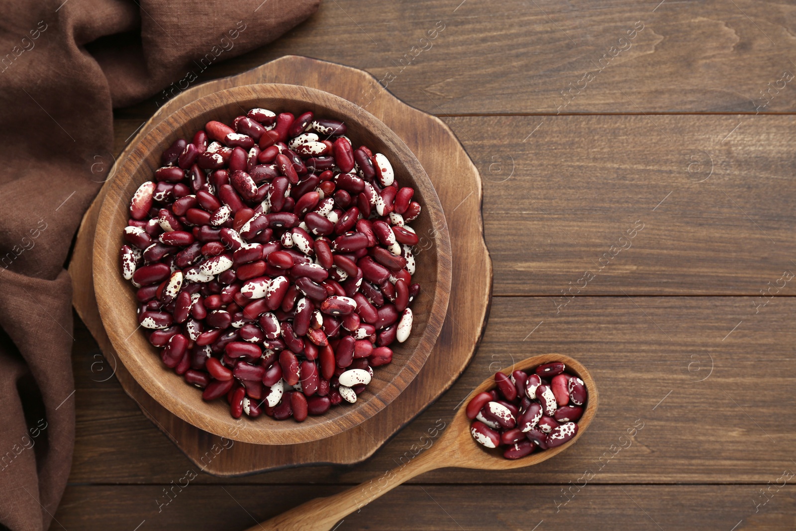 Photo of Bowl and spoon with dry kidney beans on wooden table, flat lay. Space for text