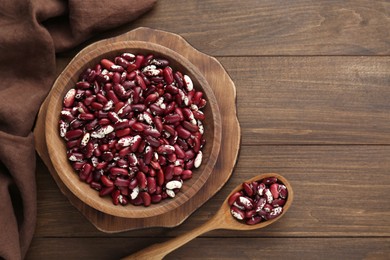 Photo of Bowl and spoon with dry kidney beans on wooden table, flat lay. Space for text