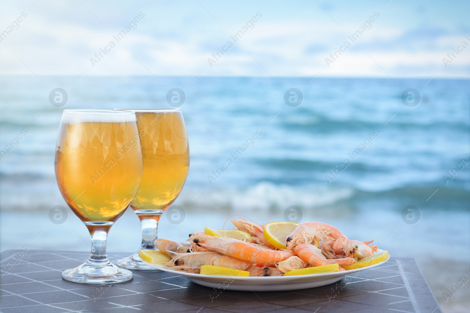 Photo of Cold beer in glasses and shrimps served with lemon on beach