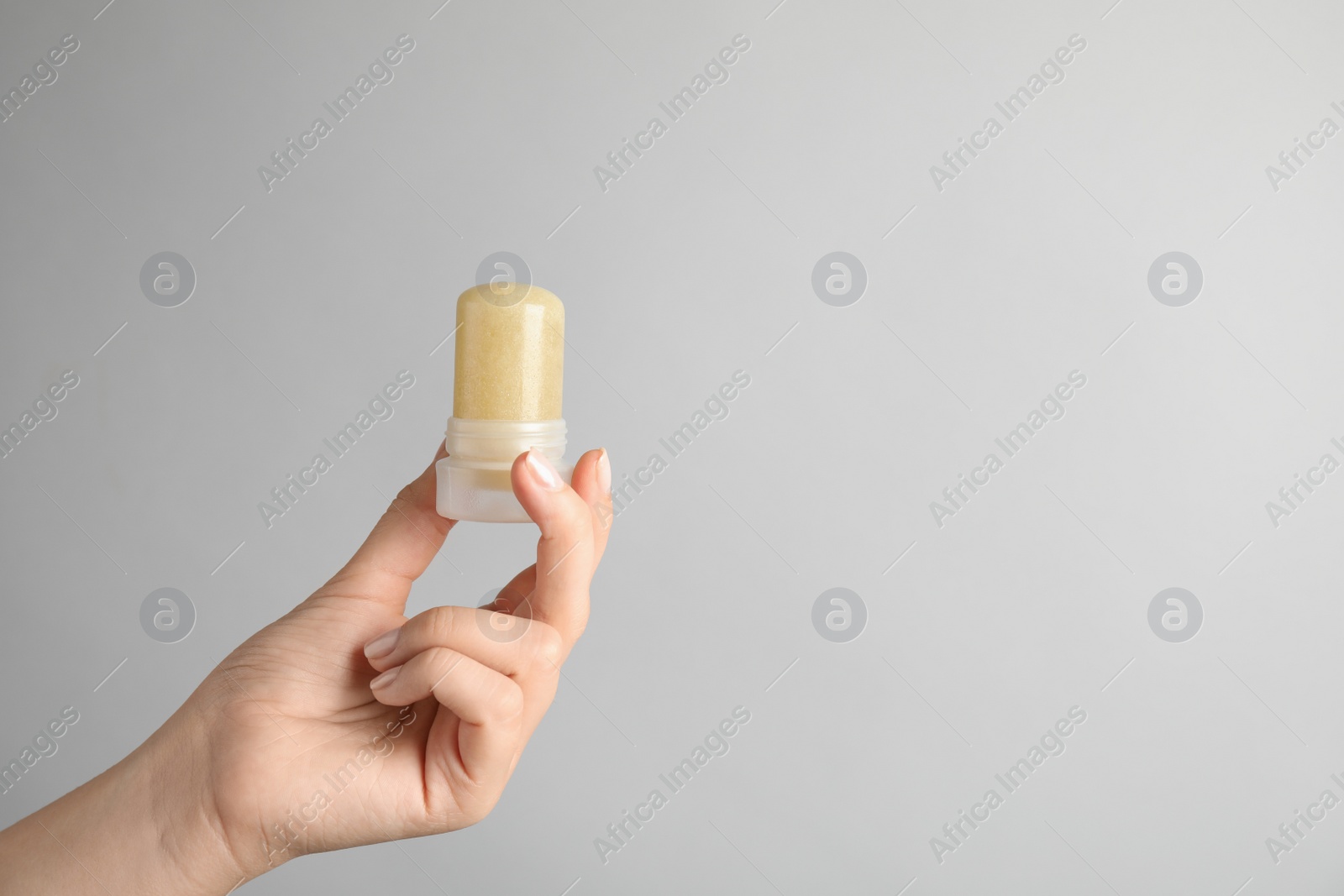 Photo of Young woman holding natural crystal alum deodorant on light grey background, closeup. Space for text