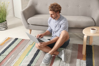 Young man with laptop sitting on floor at home