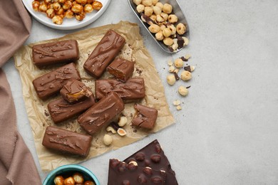 Photo of Delicious chocolate candy bars and nuts on light table, flat lay. Space for text