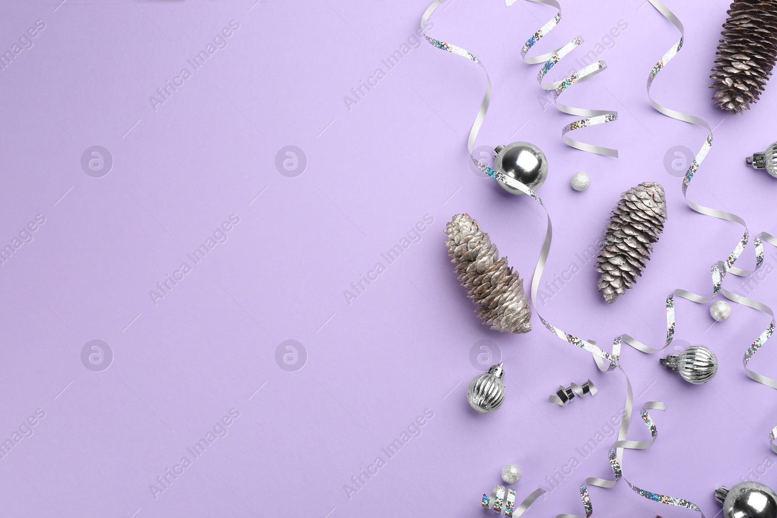 Photo of Silver serpentine streamers, Christmas balls and pine cones on violet background, flat lay. Space for text