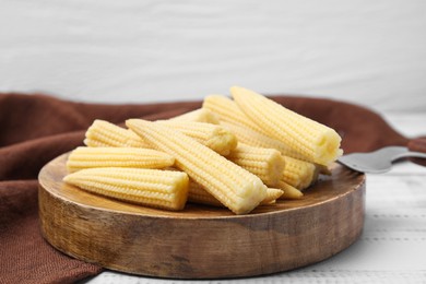 Photo of Pickled baby corn and fork on white wooden table, closeup