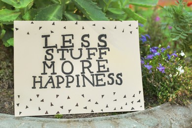 Card with phrase Less Stuff More Happiness on stone planter outdoors