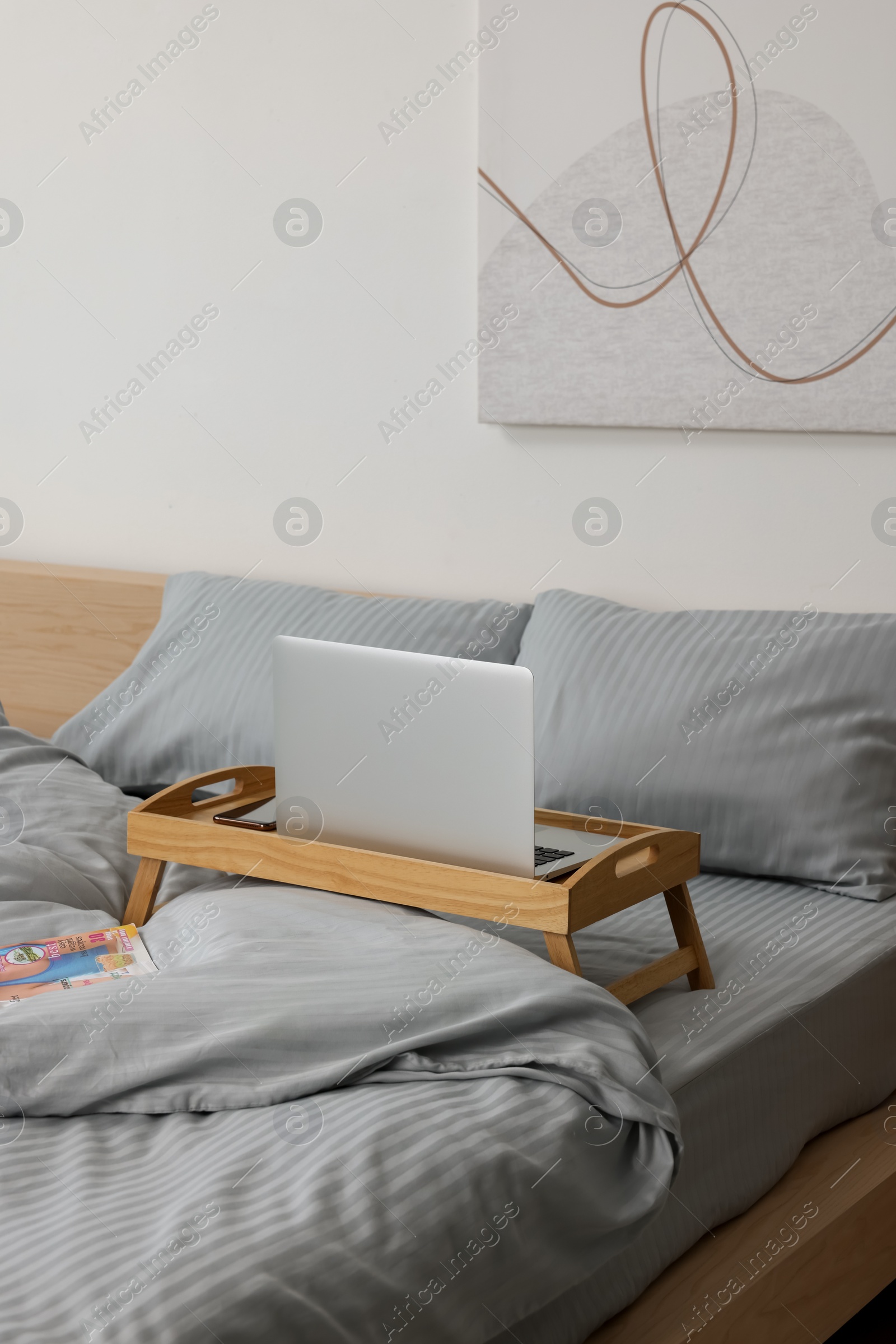 Photo of Wooden tray table with laptop and smartphone on bed indoors