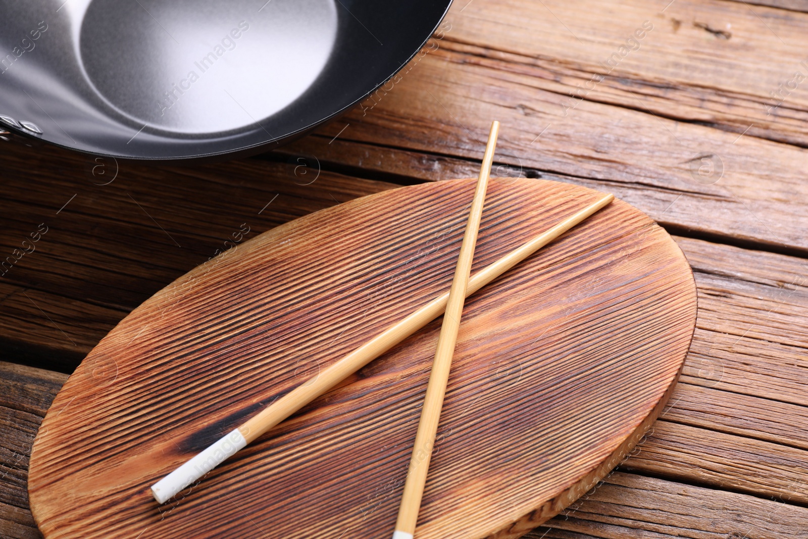 Photo of Serving board with chopsticks and iron wok on wooden table, closeup