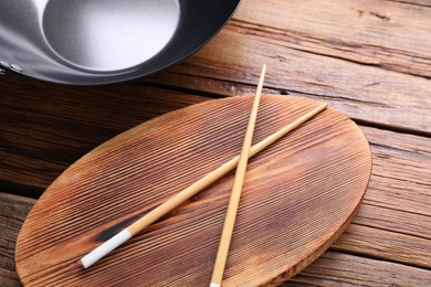 Serving board with chopsticks and iron wok on wooden table, closeup