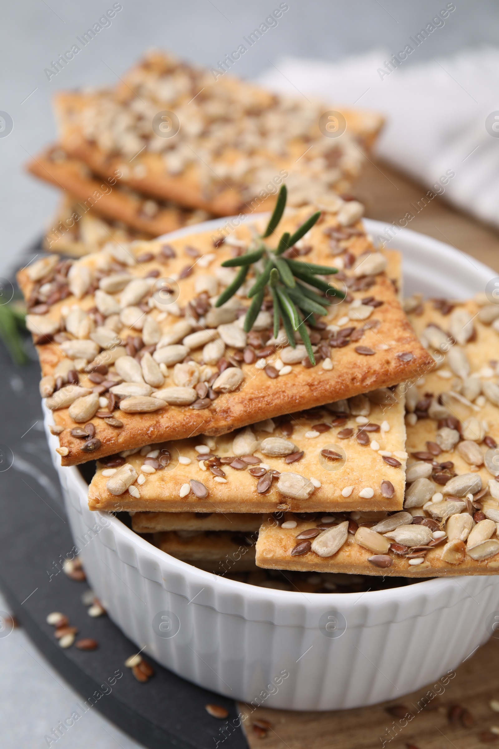 Photo of Cereal crackers with flax, sunflower, sesame seeds and rosemary in bowl on table, closeup