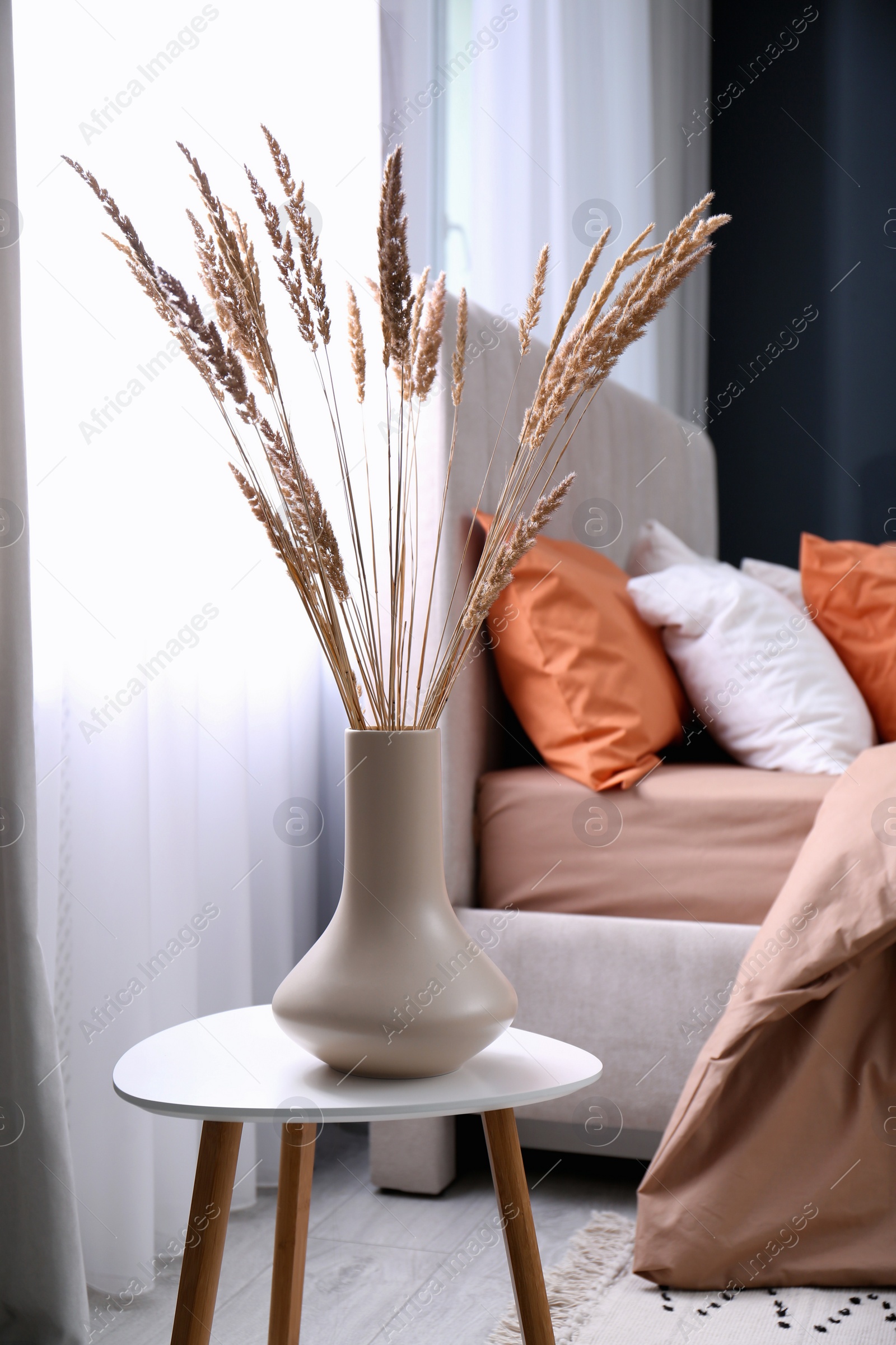 Photo of Vase with decorative dried plants on table in bedroom. Interior design
