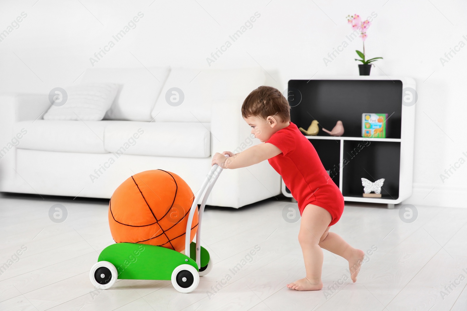 Photo of Cute baby playing with toy walker and ball at home