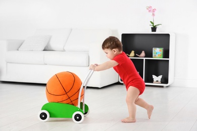 Cute baby playing with toy walker and ball at home