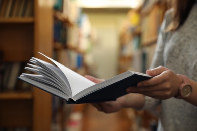 Photo of Woman holding open book in library, closeup