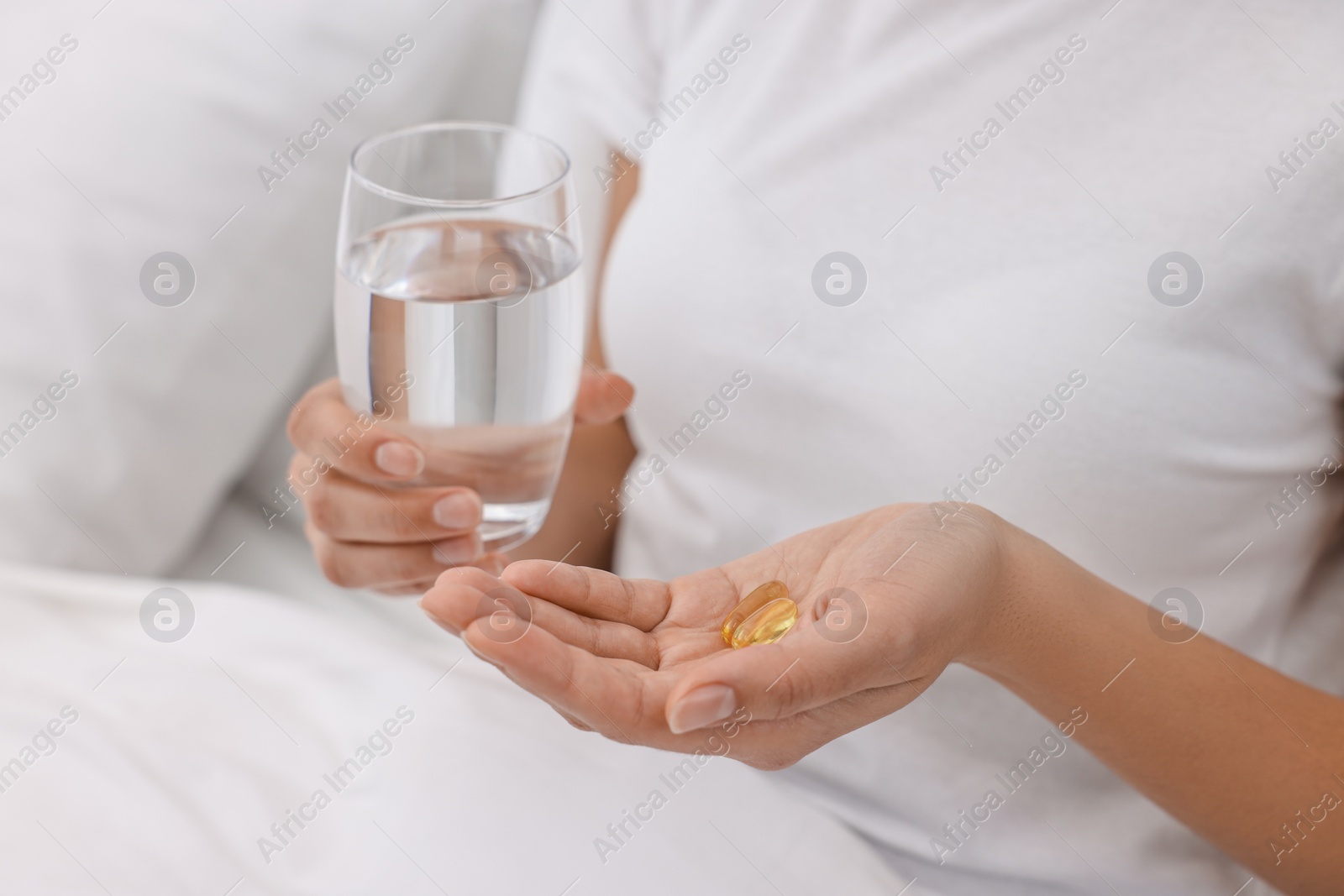 Photo of Woman with vitamin pills and glass of water in bed, closeup