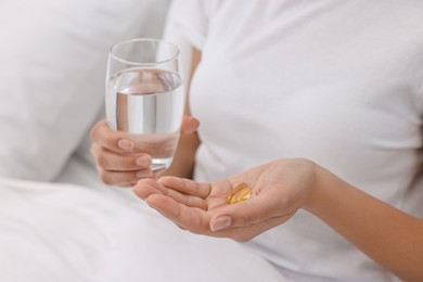 Woman with vitamin pills and glass of water in bed, closeup