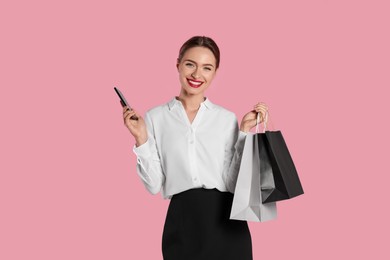 Photo of Happy young woman with shopping bags and smartphone on light pink background. Big sale