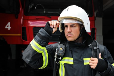 Photo of Portrait of firefighter in uniform and helmet near fire truck at station