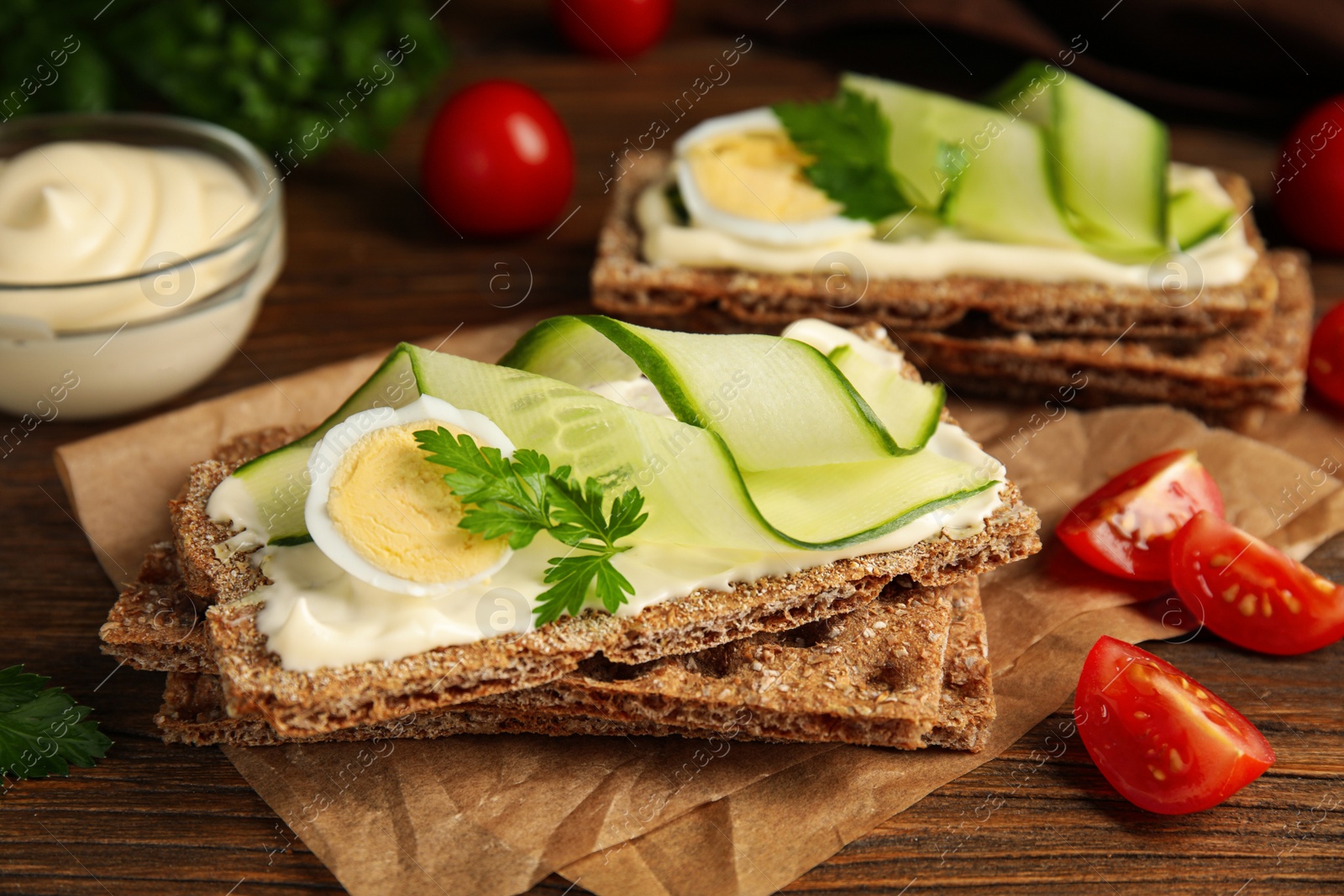 Photo of Fresh rye crispbreads with quail egg, cream cheese and cucumber slices on wooden table, closeup